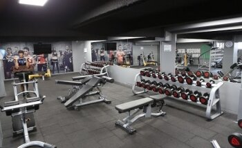 Salle de sport avec appareils de musculation, haltères, racks de poids et bancs.