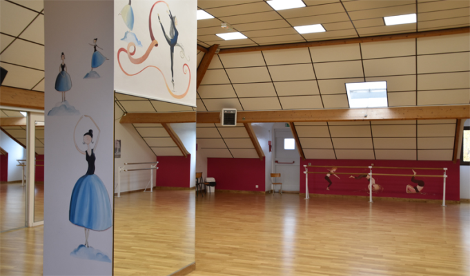 Salle de danse avec barres, miroirs, mur rouge et parquet.