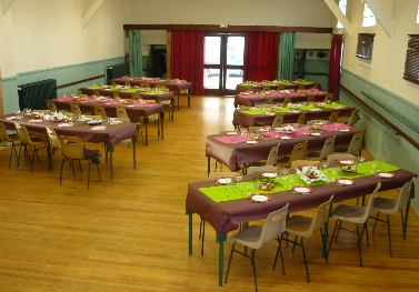 Salle avec tables, chaises, nappes, sets de table, verres et fleurs.