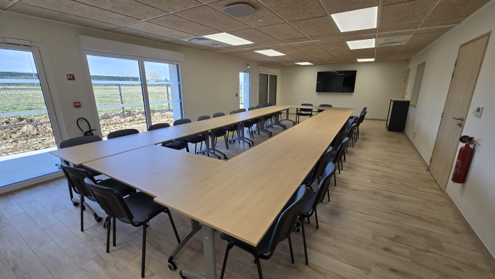 Salle de réunion avec table, chaises, écran et extincteur.
