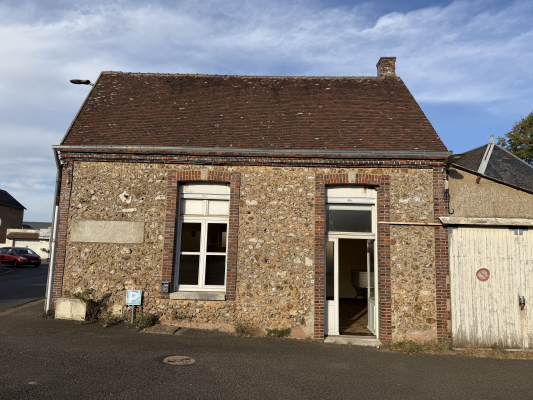 Bâtiment en pierre avec toit en tuiles, porte blanche ouverte, fenêtre à droite, porte de garage blanche à gauche.