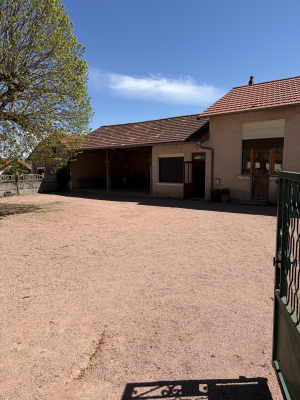 Maison avec cour en gravier, arbre, portail et barbecue.