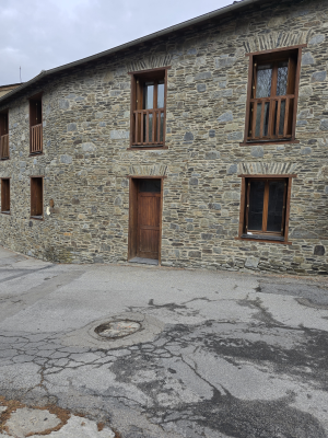 Maison en pierre avec trois fenêtres et une porte en bois, cour asphaltée fissurée.