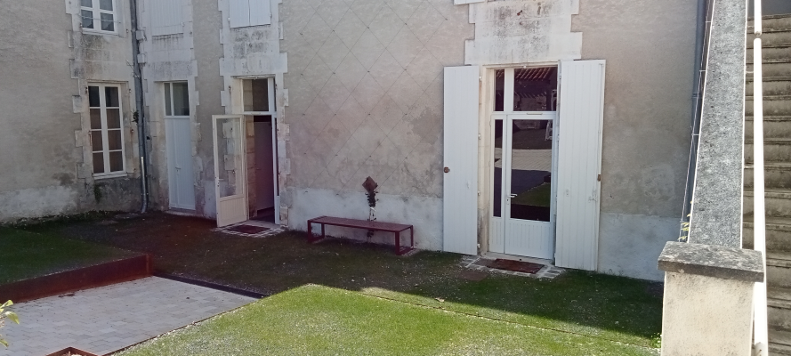 Bâtiment avec portes ouvertes, banc, pelouse et allée en béton.