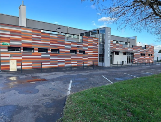 Bâtiment avec façade en briques colorées, parking et panneau "Gymnase".
