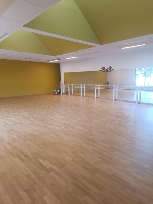 Salle avec parquet, barres de ballet, éclairage et murs jaunes.