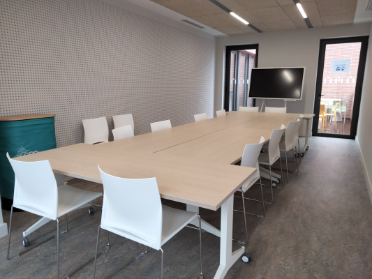 Salle de réunion avec table, chaises, écran et porte vitrée.