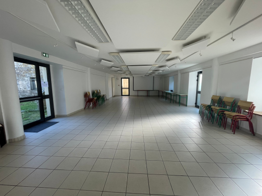 Salle vide avec portes, chaises, plantes et lumières au plafond.