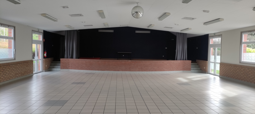 Salle avec scène, projecteurs, rideaux, portes vitrées et éclairage au plafond.