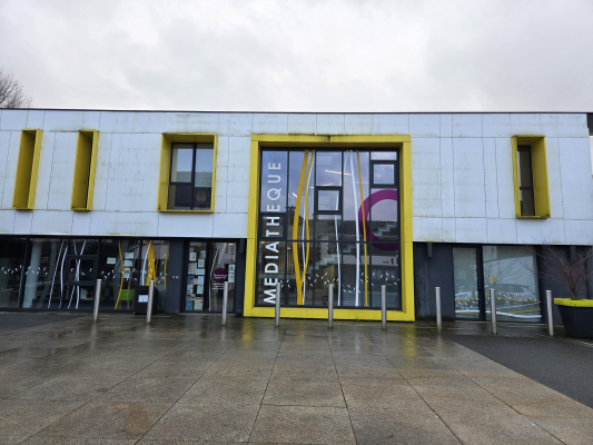 Bâtiment avec façade blanche et jaune, grandes vitres, entrée principale marquée "Médiathèque".
