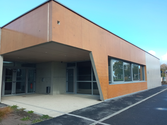 Bâtiment avec façade en bois, porte en verre et parking.