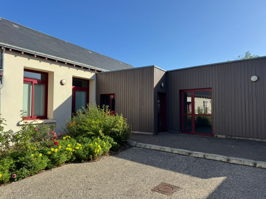 Bâtiment avec portes et fenêtres rouges, allée de gravier, plantes et pot de fleurs.
