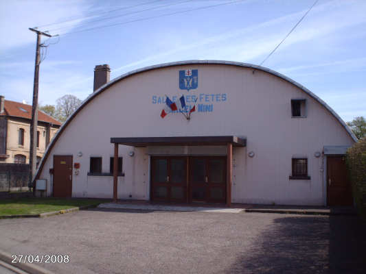 Bâtiment avec entrée centrale, portes latérales, blason et enseigne "Salle des fêtes mini".