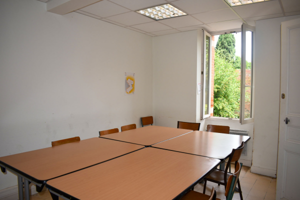Salle avec tables, chaises, fenêtre, éclairage et tableau.