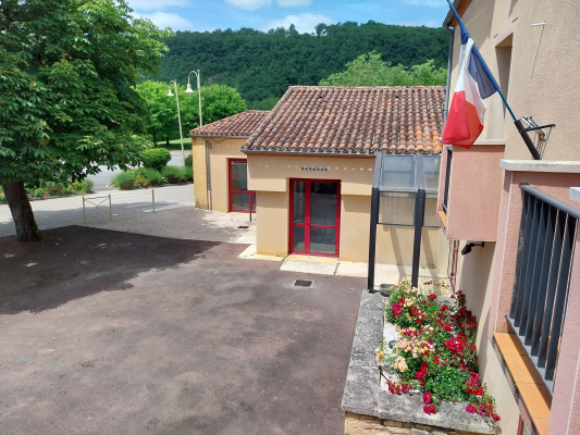 Bâtiment avec toit en tuiles, porte rouge, drapeau français, fleurs, gare, et environnement verdoyant.