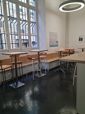 Salle avec tables, tabourets, chaises, vitres et luminaire rond au plafond.