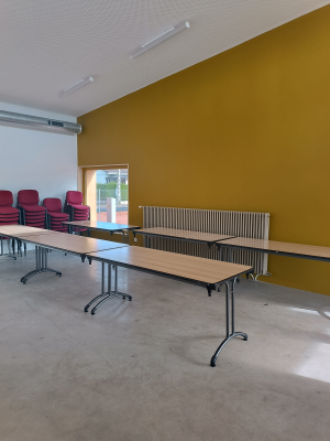 Salle avec tables, chaises, radiateurs et tableau blanc.