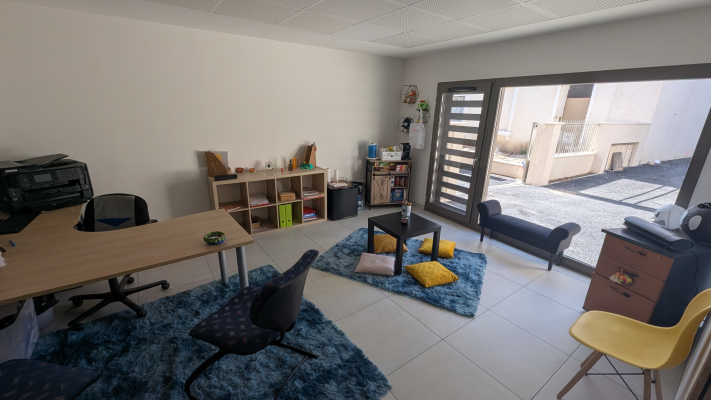 Salle avec table, chaises, étagères, canapé, tapis, coussins, classeur et porte vitrée.
