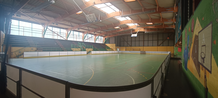 Salle polyvalente avec terrain, gradins, panneaux sportifs et éclairage.