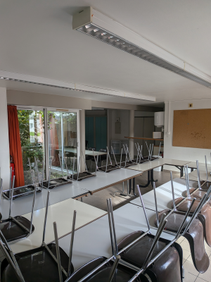 Salle de classe avec tables, chaises, tableau blanc et projecteur.