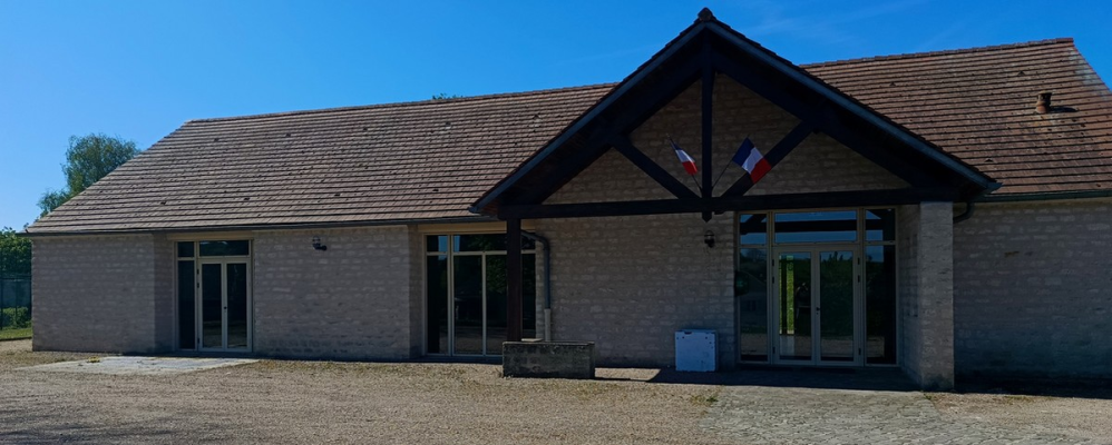 Bâtiment avec toiture en tuiles, murs en briques, grandes fenêtres et portes vitrées. Deux drapeaux français.