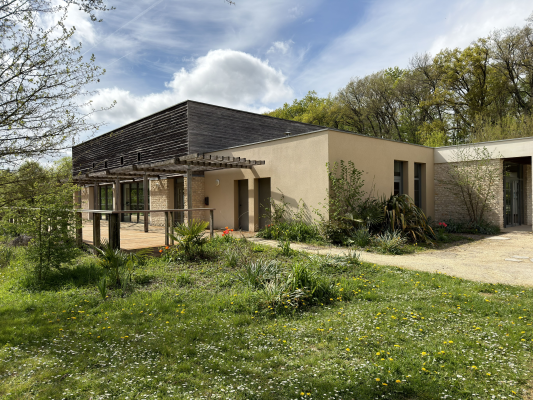Maison moderne avec toit plat, murs beiges, grandes fenêtres et jardin bien entretenu.