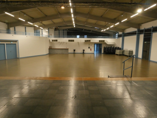 Grande salle avec sol lisse, éclairage suspendu, rampes et escalier métallique.
