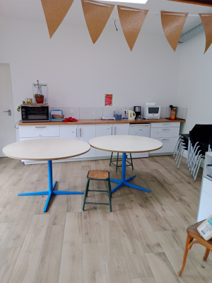 Salle avec tables rondes, tabourets, cuisine équipée et décorations en papier.