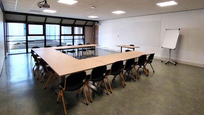 Salle avec tables en U, chaises, tableau blanc et vidéoprojecteur.