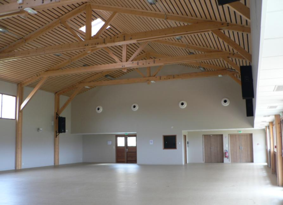 Grande salle avec poutre en bois, sol nu, portes et écrans.