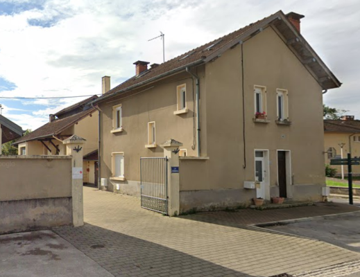 Maison mitoyenne, portail en métal, allée pavée, antenne TV, muret.