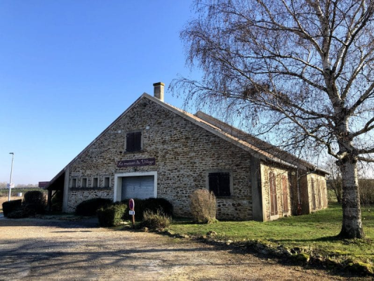 Bâtiment en pierre avec un panneau, un arbre nu, des buissons et une allée en gravier.
