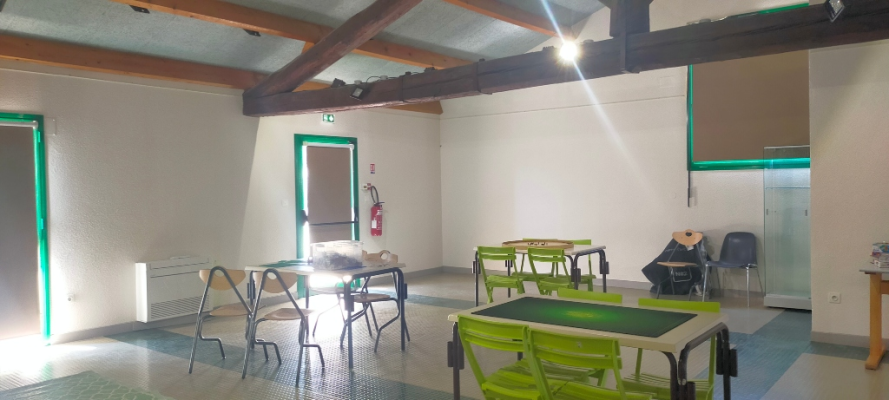 Salle avec tables, chaises, radiateur, extincteur, porte-manteau et armoire.