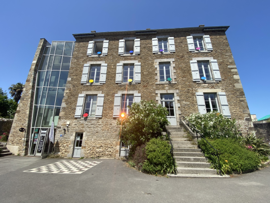 Bâtiment en pierre avec plusieurs fenêtres, portes vitrées, escaliers et fleurs.