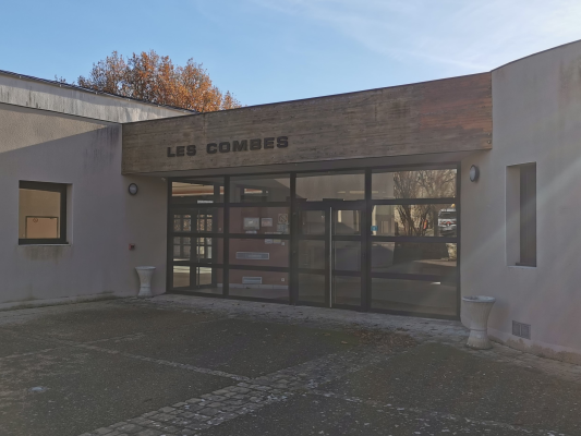 Entrée d'immeuble avec portes vitrées, enseigne et urinoirs extérieurs.