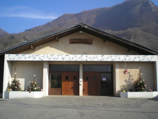 Bâtiment avec porte en bois double, porte plus petite, décorations florales, enseigne, montagnes en arrière-plan.