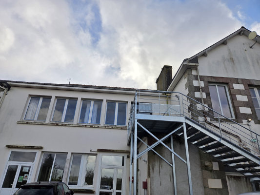 Bâtiment avec escaliers extérieurs et voitures garées.