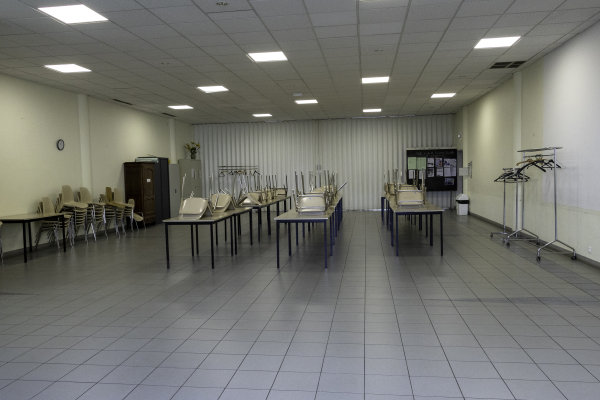 Salle de classe avec tables, chaises, projecteurs, armoire et supports pour vêtement.