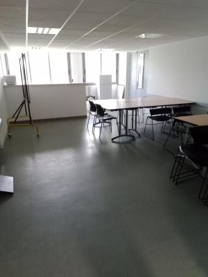 Salle avec tables, chaises, chevalet et fenêtres.