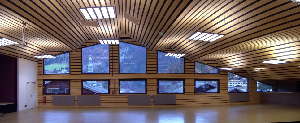 Salle spacieuse avec grandes fenêtres, projecteurs et bancs.