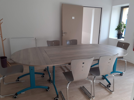 Salle de réunion avec table ovale, chaises, porte-manteau, radiateur et plante.