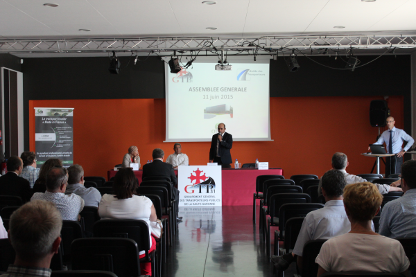 Assemblée générale avec écran, podium, projecteur, chaises et public.