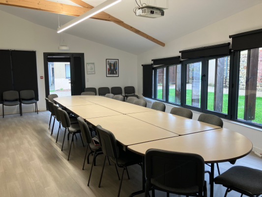 Salle de réunion avec table, chaises, vidéoprojecteur et grandes fenêtres.