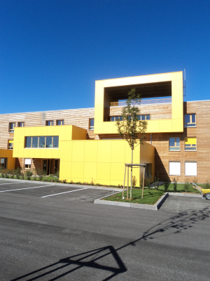Immeuble jaune avec arbre, parking et vélo.