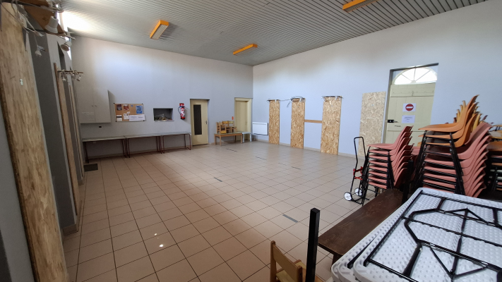 Salle avec tables, chaises empilées, chariot, et matériel de rangement.