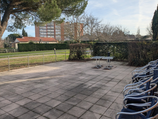 "Espace extérieur avec tables, chaises, terrain gazonné et bâtiment en arrière-plan."