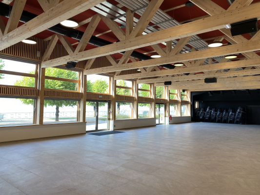 Salle spacieuse avec chaises, grandes fenêtres et structure en bois.