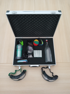 Valise ouverte contenant des lunettes de protection, une bouteille, un ballon, un spray et des documents.