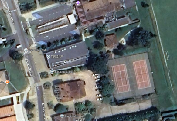 Vue aérienne d'un complexe sportif avec terrain de tennis, parking, et plusieurs bâtiments incluant un musée et une mairie.