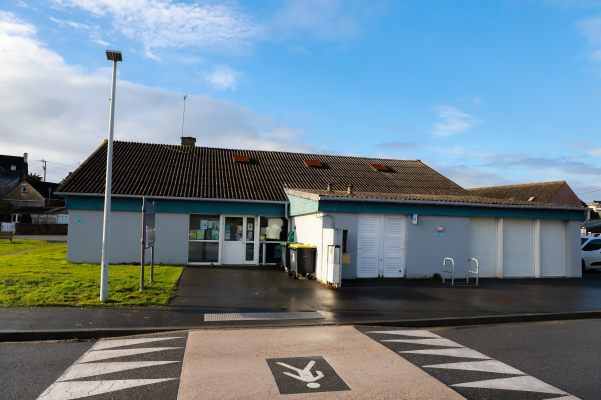 Bâtiment avec toit en pente, entrées et parking, marque au sol.